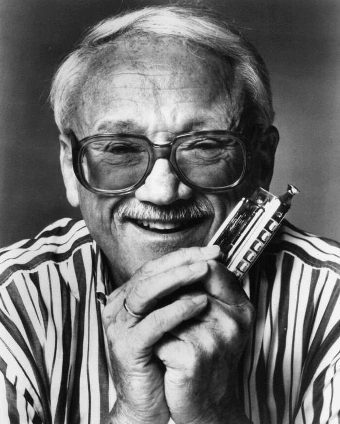 Toots Thielemans souriant, harmonica à la main, chemise rayée