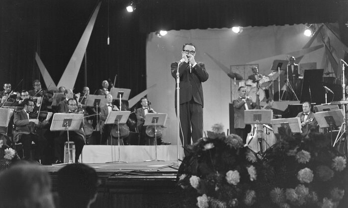 Toots Thielemans jouant de l'harmonica devant un orchestre, sur scène