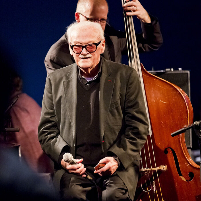 Toots Thielemans en concert, assis, contrebassiste à l'arrière-plan